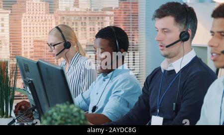 African customer service representative working on multiracial team of modern call center. Teamwork activity desk in busy office. Stock Photo