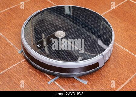 Black robot vacuum cleaner on tile in the kitchen Stock Photo