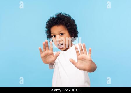 Child phobia. Portrait of scared little boy looking terrified panicked at camera and showing stop gesture as if trying to defend himself, screaming in Stock Photo