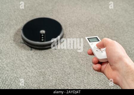 male hand turns on the robot vacuum cleaner using the remote control Stock Photo