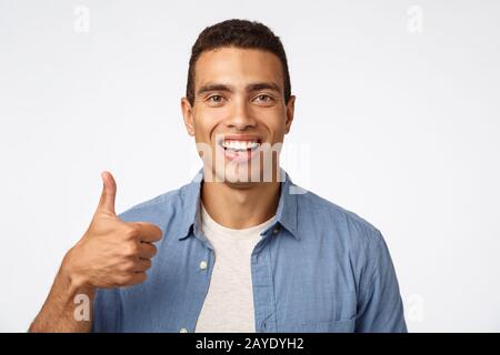 Supportive good-looking hispanic man showing thumbs-up, like idea, smiling happy, approve or recommend product, give positive fe Stock Photo