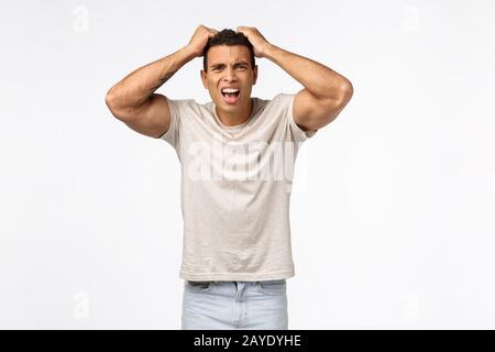 Disappointed athletic man in t-shirt, grab head and pull hair bothered, frowning grimacing shocked and frustrated, lost huge mon Stock Photo