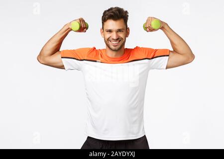 Sport, diet and healthy lifestyle concept. Handsome smiling, happy sportsman enjoy workout, proudly showing his muscles, lift ar Stock Photo