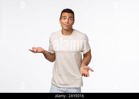 Clueless handsome young hispanic muscular man in casual t-shirt, shrugging, spread arms sideways, smirk and look indecisive, don Stock Photo