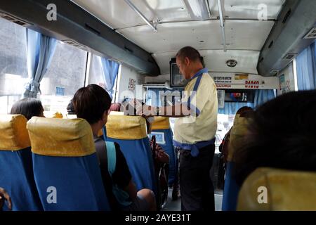 Mandaluyong City, Philippines - February 13, 2020: Bus conductor gives a passenger his bus ticket after paying for the fare. Stock Photo