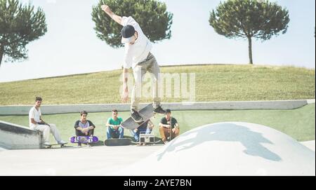 Young skater jumping with skateboard while friends watching him in background - Sporty guy performing tricks and skills  - Extreme sport, youth lifest Stock Photo