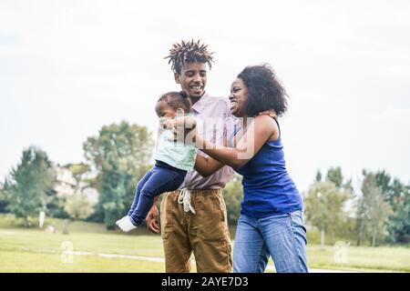 Happy african family having fun outdoor  in public city park - Dad, mum and daughter enjoying tender moments together - Love and parenthood concept - Stock Photo