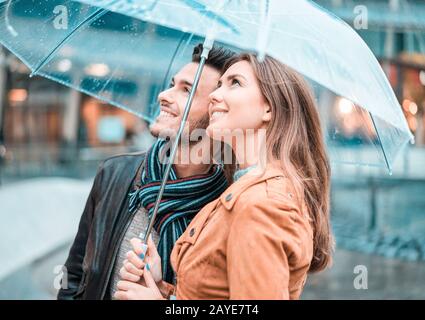 Young happy couple under the rain day covering with transparent umbrella in city center - Lovers traveling Europe during fall season - Love concept - Stock Photo