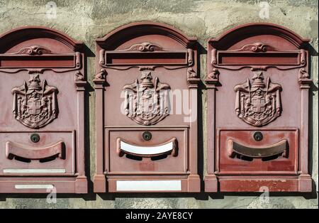 Old vintage mailboxes in Italy. Metal red mailboxes on grey facade. Stock Photo