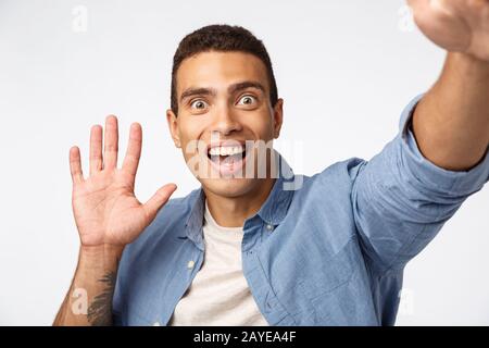 Surprised and impressed man didnt expact see someone as holding camera, waving hand in hello or hi gesture, pop eyes fascinated, Stock Photo