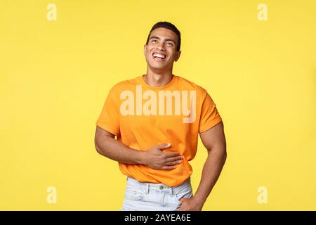 Man feeling pain abdominal muscles as laughing out loud from hilarious comedy or joke, chuckling, touching stomach and look up s Stock Photo