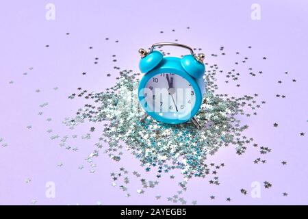 Blue vintage alarm clock on a lavender background with silver glitter. Stock Photo
