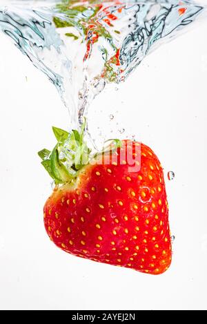 Strawberry falls deeply under water with a big splash. Fruit sinking in clear water on white background Stock Photo