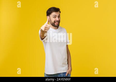 Young happy man with thumbs up sign in casuals isolated on yellow background Stock Photo