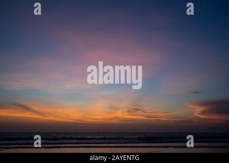 Orange clouds at ocean sunset with the waves breaking the seashore Stock Photo