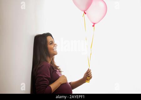 Pregnant woman smiling at the pink balloons in her hand. Stock Photo