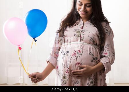 Pregnant woman holding balloons in hand and smiling at her baby bump. Stock Photo