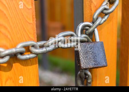 A padlock on a steel chain hangs and locks the doors of a yellow new wooden fence Stock Photo