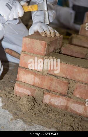 Mason builds brick wall with small bricks and masonry hammer - close-up Stock Photo