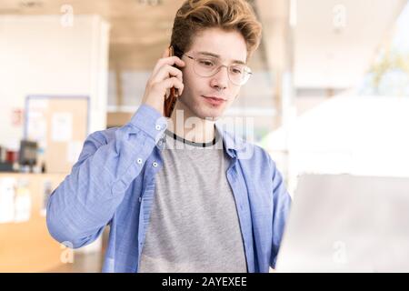 Young man with piercings talking on a cell phone with a serious expression working in a coworking Stock Photo