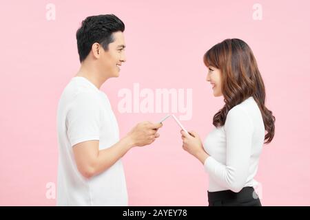 Face-to-face conversation. Excited man and woman talking holding smartphones looking at each other standing over pink Background. Stock Photo
