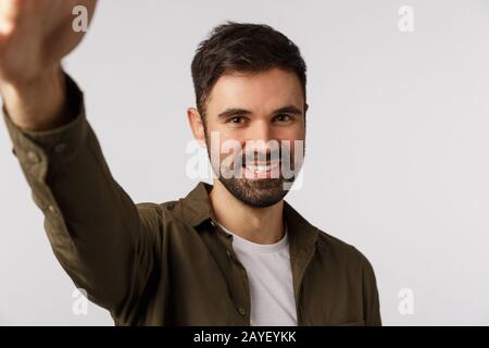 Handsome cheerful bearded man in coat want upload new photo gay dating application, hold smartphone with arm and smiling camera, Stock Photo