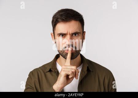 You better stay quiet about this. Aggressive, angry, displeased caucasian bearded male in coat, shushing demand keep silent, hus Stock Photo