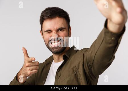 Cheeky and carefree confident handsome bearded guy, taking selfie as holding smartphone one hand, making pointing gesture as che Stock Photo