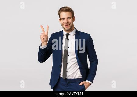 Charming, wealthy good-looking blond bearded guy in classic suit, showing peace sign, smiling joyfully, telling team they made d Stock Photo