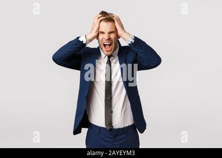 Distressed young businessman lost all money, feeling depressed and let down, frowning upset, screaming in rage, holding hands on Stock Photo