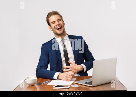 Man watching funny videos online while sitting office during worktime. Attractive businessman in classic suit sitting desk laugh Stock Photo