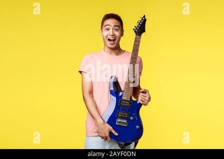 Handsome young musician playing the guitar and singing, isolated on yellow background Stock Photo