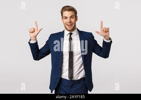 Surprised and glad, excited smiling bearded businessman, male entrepreneur in suit, showing product banner, pointing fingers up Stock Photo