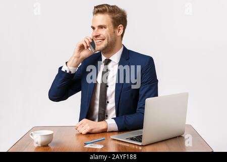 Handsome cheerful blond male entrepreneur sitting in office, calling business partner, contact manager, making order via mobile, Stock Photo