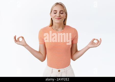 Patience key to success. Attractive calm, relieved blond caucasian woman in striped t-shirt, close eyes and smiling gather relaxation, spread hands Stock Photo