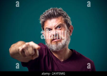 A portrait of angry bearded man in red t-shirt pointing finger at camera. People and emotions concept Stock Photo