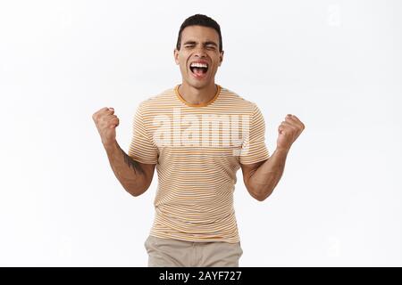 Pumped happy guy achieve success, celebrating, shouting from happiness with closed eyes and clenched fists, got approval, scream yes satisfied Stock Photo