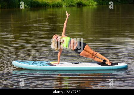 Young blonde woman planking sideward on SUP in water Stock Photo