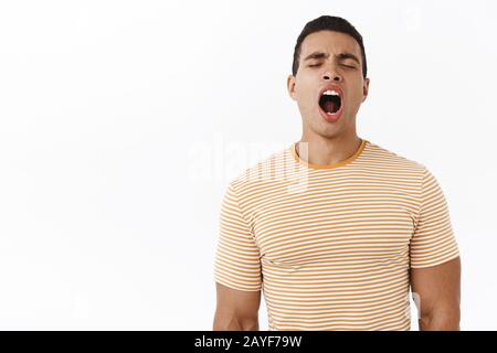 So tired. Attractive young masculine male in striped t-shirt, yawning with closed eyes and opened mouth, waking up early, feeling bored or havent Stock Photo