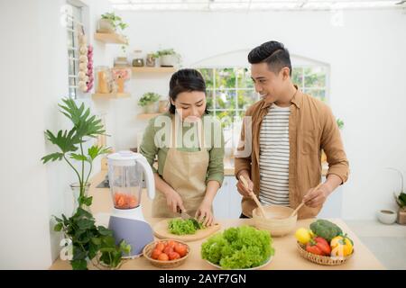 Portrait of happy young Asian couple cooking together in the kitchen at home. Stock Photo