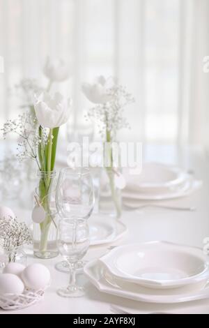 Happy Easter! Decor and table setting of the Easter table with white tulips and dishes of white color.  Selective focus. Stock Photo