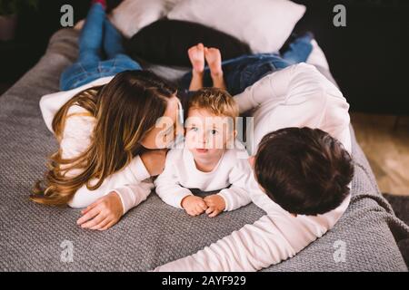 Happy family having fun lying down on bed at home. Happy Family In Bed. Mom dad and son lie on bedroom at within doors. father, Stock Photo