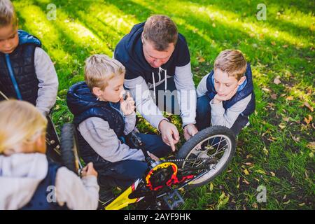 Father day. A large friendly family father and sons together actively relax in the fresh air. Dad teaches sons to repair bicycle