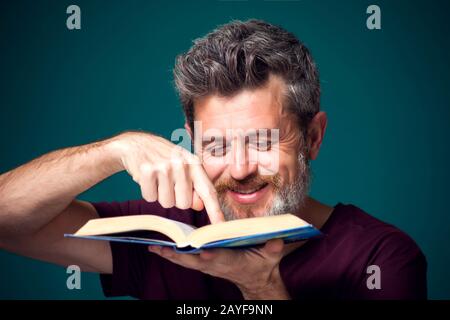 A portrait of bearded man in red t-shirt holding opened book. People, education and searching concept Stock Photo