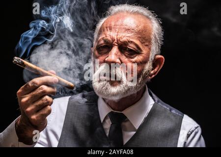 Portrait of serious senior man who is smoling cigar. Stock Photo