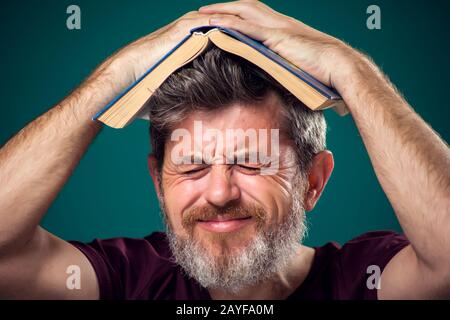 A portrait of bearded man in red t-shirt holding opened book on head. People, education and searching concept Stock Photo