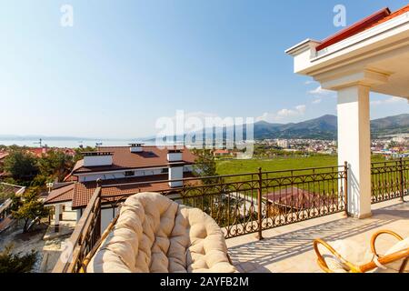 Large beautiful rich spacious veranda in the cottage with views of the mountains and the sea. Soft summer wicker sofas and armchairs. Veranda with bea Stock Photo