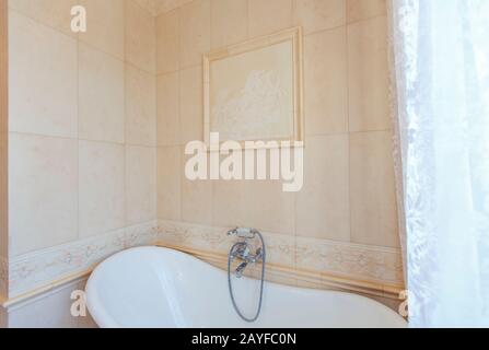 Classic bathroom in beige tones. Curved bath tub. Large beige tile. White tiles on the floor. Twisted chandelier. elegant expensive plumbing Stock Photo