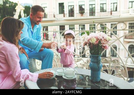 beautiful family on the balcony of the hotel enjoys the city view, in the nightgowns breakfast at the hotel, happy young parents with a child Stock Photo