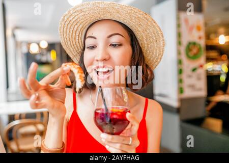 Happy Asian woman in hat eating local Spanish cuisine grilled seafood Stock Photo